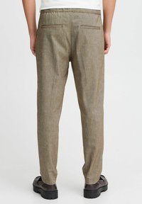 Man wearing beige textured pants and dark brown shoes, shown from the back against a plain light background.