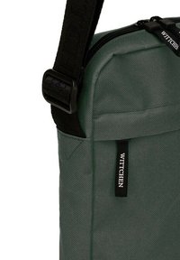Grüne Stoff-Schultertasche mit texturierter Oberfläche, schwarzem verstellbarem Tragegurt, Reißverschluss und einem WITTCHEN-Logoetikett auf der Vorderseite.