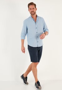 Camicia a maniche lunghe blu chiaro con colletto a bottoni, pantaloni corti navy e sneakers grigie con lacci neri. Design semplice, vestibilità casual.