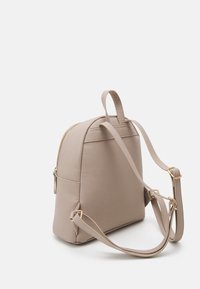 Mochila sintética beige con forma estructurada, detalles metálicos dorados y correas ajustables. Cuenta con un compartimento principal con cremallera.