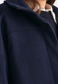 Giacca in misto lana blu navy con colletto, caratterizzata da una texture morbida e dettagli di cucitura visibili. Il design include una vestibilità comoda e revers.