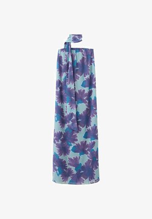 Mujer con vestido largo sin tirantes con gran estampado floral en tonos púrpura y azul, combinado con sandalias plateadas, de pie frente a un fondo liso.