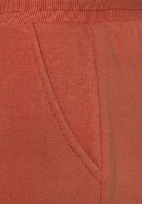 Tela de jersey roja con un bolsillo y cintura acanalada. La textura es suave, mostrando variaciones sutiles en el patrón del hilo.