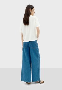 Witte t-shirt met korte mouwen, gecombineerd met wijde blauwe denim jeans. De jeans hebben achterzakken en een casual pasvorm.