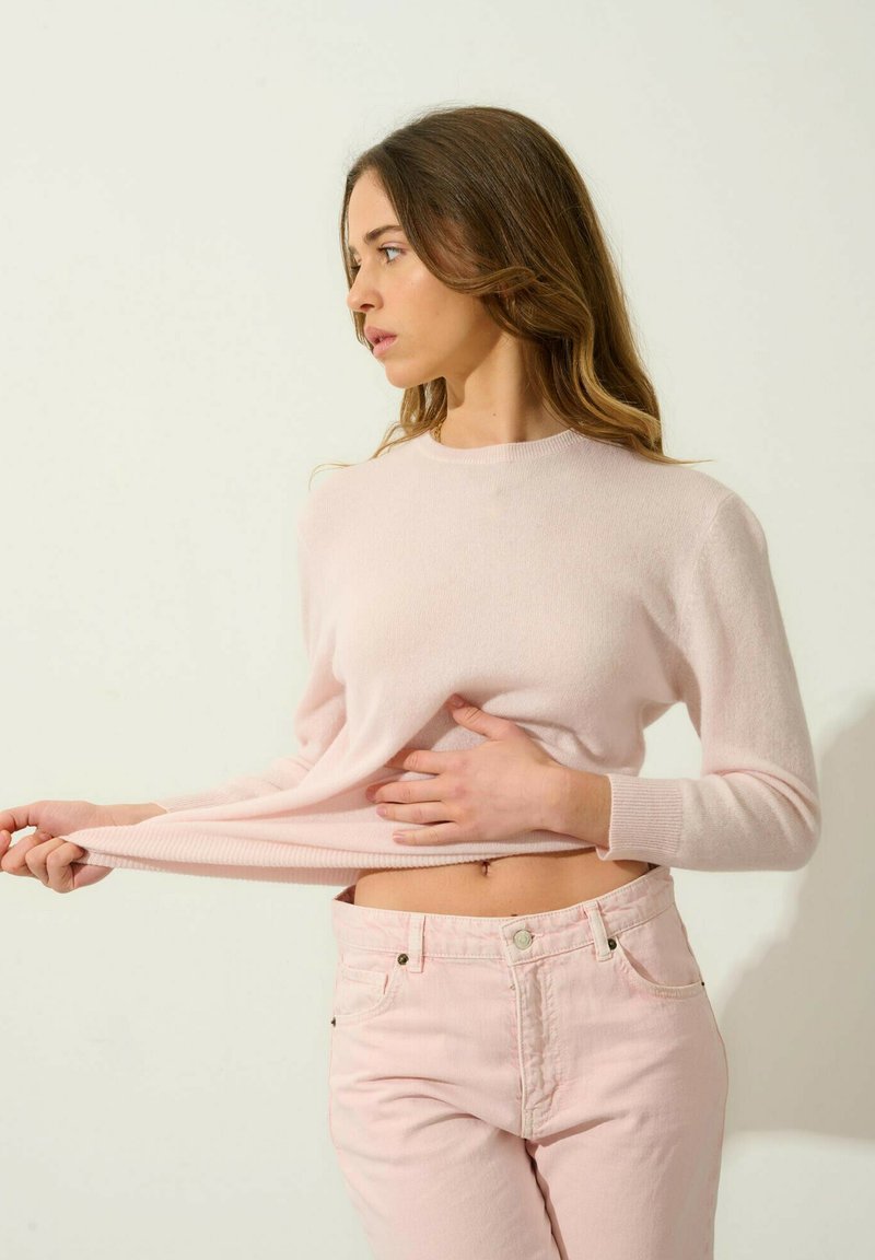 Jasnoróżowy sweter z dzianiny z okrągłym dekoltem i długimi rękawami, w parze z jasnoróżowymi dżinsami, obie części mają miękką teksturę.