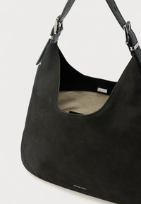 Czarna skórzana torba na ramię Michael Kors z regulowanym paskiem i beżowym materiałowym wnętrzem widocznym przez szerokie zapięcie.