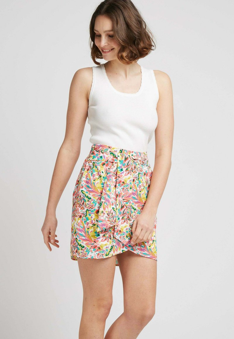 Jupe portefeuille imprimée florale dans des teintes vives de rose, vert et jaune. Tissu léger, texture douce, avec un détail de taille nouée et une longueur courte.