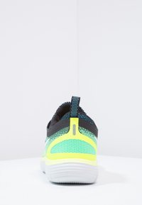 Zelená a černá sportovní bota s texturovaným síťovaným svrškem, reflexními akcenty a polstrovanou podešví, která má poutko pro snadné obutí.