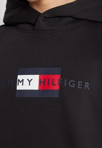 Black hoodie featuring a rectangular logo with navy, white, and red sections, displaying "TOMMY HILFIGER" in bold lettering.