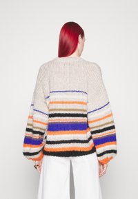 Pull en tricot avec manches ballon surdimensionnées. Présente un motif à rayures horizontales en orange, bleu, noir et couleurs neutres. Tissu texturé.