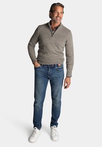 Grijze gebreide trui met een hoge hals, gedragen over een geruit shirt, gecombineerd met blauwe jeans en witte sneakers. Eenvoudig ontwerp met geribbelde manchetten.