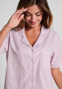 Lichtroze overhemd met korte mouwen en een knoopsluiting aan de voorkant, met witte diamanten patronen en een borstzak. Soepele stoftextuur.