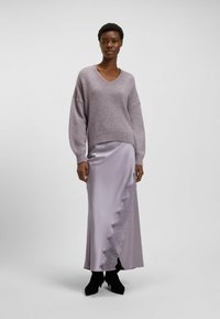Liliowy sweter dzianinowy z dekoltem w serek i opadającymi ramionami, w połączeniu z długą satynową spódnicą w odcieniu liliowym, wyróżniającą się koronkowym wykończeniem i falbaniastym brzegiem.