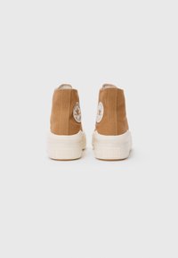 Tans canvas hoge sneakers met witte rubberen zolen, met een rond logopatch op de achterkant en gestikte details bij de naden.