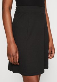 Jupe noire en jersey avec une taille élastiquée et une coupe évasée. Texture lisse avec des coutures visibles au niveau de l'ourlet. Ajustement réglable.