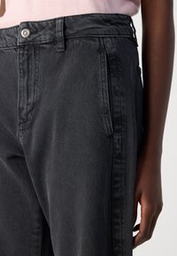 Sorte denimbukser med høy midje, sidelommer og en avslappet passform. Strukturert stoff med en subtil glans og synlige sømmer.