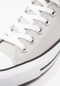 Gray suede sneaker featuring white laces, metal eyelets, and a textured white rubber sole with black accents near the bottom.