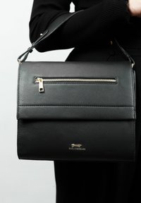 Zwarte leren handtas met een vouwbovenkant, voorzak met rits en zilverkleurige hardware. Glad textuur met geperst logo-detail.