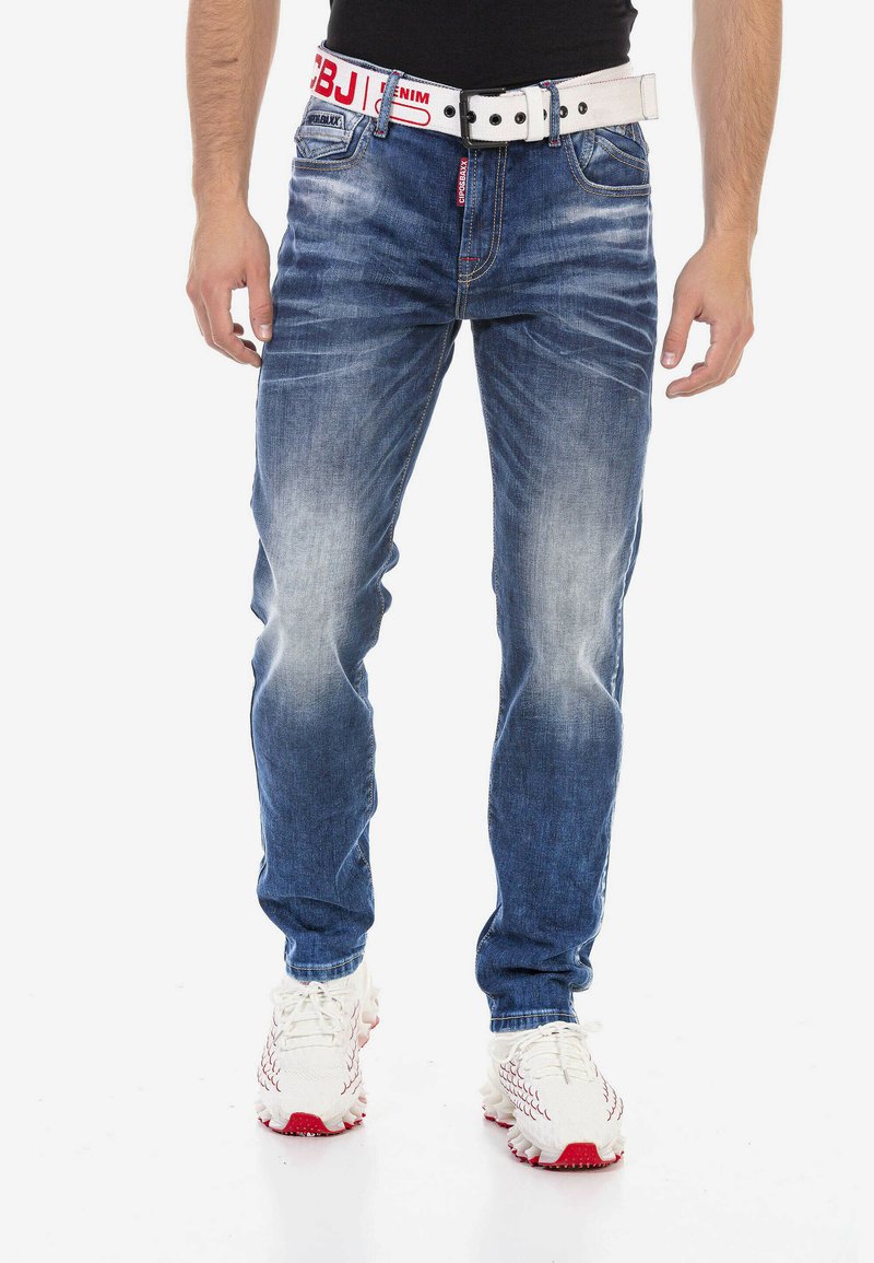 Helle blaue Jeans im tapered Fit mit ausgewaschenen Stellen. Kombiniert mit einem breiten, weißen Gürtel mit roter Schrift und Knöpfen.