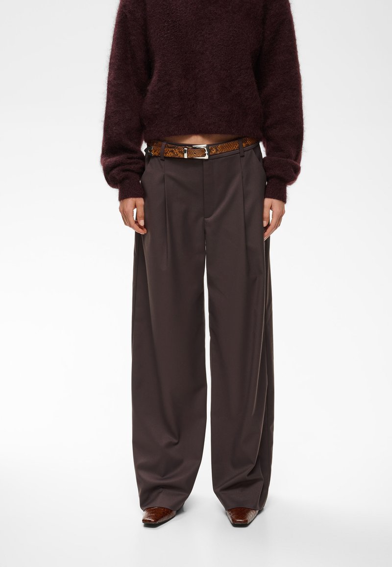 Personne portant un pantalon large marron foncé, un pull court bordeaux duveteux, une ceinture marron texturée et des chaussures marron pointues.