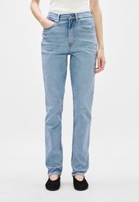 Ανοιχτό μπλε τζιν παντελόνι με ίσια γραμμή, υψηλή μέση, πέντε τσέπες και διακριτικό ξεθώριασμα, συνδυασμένο με μαύρα φλατ.