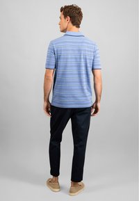 Világoskék pólóing vízszintes csíkokkal, sötét nadrággal és bézs slip-on cipővel párosítva, hátulról nézve, szürke háttér előtt.