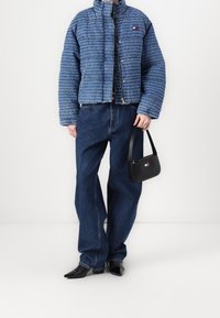 Blå kviltad jacka med textmönster, tillsammans med lösa mörkblå jeans, spetsiga svarta skor och en liten svart handväska.