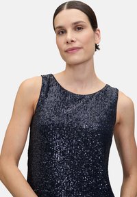 Robe sans manches navy en tissu pailleté, avec un col rond et une silhouette ajustée. Texture lisse et surface brillante et réfléchissante.