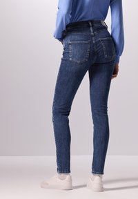 Jeans ajustados de color azul oscuro con bolsillos traseros, de corte slim, con una cinturilla de altura media, y combinados con zapatillas blancas.