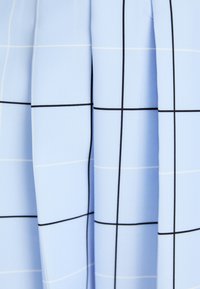 Ljusblått tyg med rutmönster; har tunna vita linjer och kontrasterande svarta linjer; slät textur som antyder en skräddarsydd design.