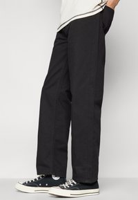 Sorte vide benbukser lavet af tekstureret stof, med sidelommer og en glat talje, parret med sorte høj-top sneakers.