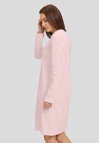 Vestido de manga larga en suave tejido rosa, con un sutil patrón en forma de chevron, corte hasta la rodilla y escote redondeado. Diseño minimalista.