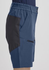 Shorts bleus avec un panneau latéral noir, taille élastique avec boutons, poches avant et une poche zippée sur le côté. Texture lisse.