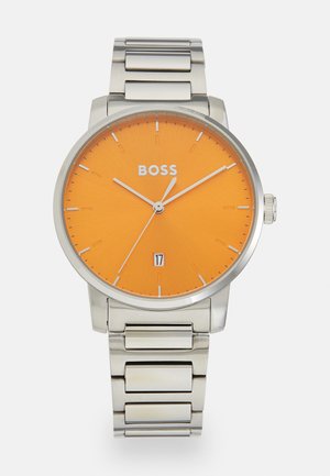 Montre-bracelet en acier inoxydable avec un cadran orange, des indices et aiguilles argentés. Présente un affichage de la date au-dessus du six et un bracelet en métal lié.