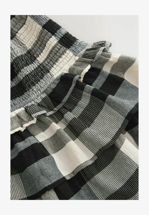 Czarna i biała materiał w kratę charakteryzuje się mieszanką gładkich i wzorzystych kwadratów oraz teksturowanym, marszczonym pasem i falbaną na krawędzi.