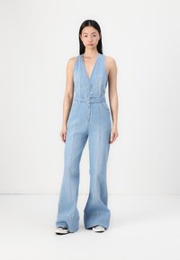 Jumpsuit en denim bleu clair avec un décolleté en V profond, deux boutons à l'avant et des jambes évasées. Comprend des coutures verticales et des poches.