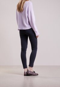 Lila gebreide trui met geribde zoom, zwarte strakke jeans en gestructureerde donkere slangenleren loafers met een strikdetail.