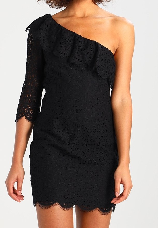 Femme portant une robe noire en dentelle à une épaule, avec un col à volants et une manche trois-quarts.