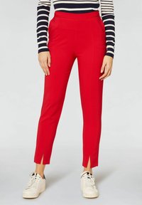 Pantalons taillés rouges avec fentes sur les côtés, fabriqués en tissu lisse. Portés avec un haut rayé bleu marine et des baskets blanches.