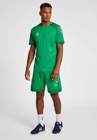Grön sportdräkt med kortärmad skjorta och matchande shorts, tillverkad av ventilerande tyg med kontrasterande detaljer och logotyp.