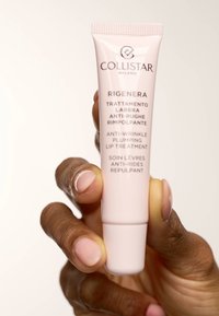 Collistar Rigenera anti-rynkor läppbehandling i en rosa tub, med tydlig text, hålls i en hand med ljus hudfärg och neutral nagellack.