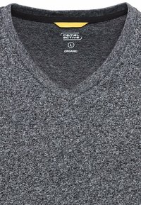 Grijze v-hals trui gemaakt van organisch materiaal. Getextureerd oppervlak met een subtiel patroon. Voorzien van een zwarte halslijn en een gele binnenlabel.