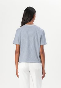 Tricou rayé din bumbac albastru și alb, cu mâneci scurte, gât rotund, croială lejeră, cusături vizibile, purtat cu pantaloni albi.