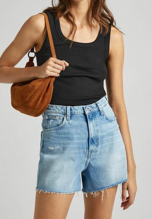 Femme portant un haut noir sans manches, un short en denim bleu clair taille haute avec des bords effilochés, et portant un sac à épaule en daim marron.