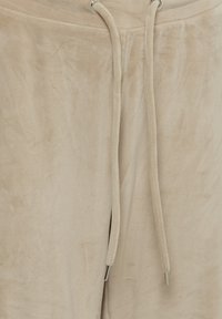 Pantalon de survêtement beige en tissu doux avec taille à cordon et embouts métalliques sur les cordons.