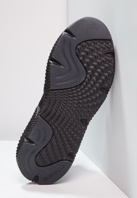 Black athletic shoe sole featuring rubber material with textured grip patterns, smooth accents, and a curved design for flexibility.