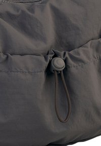 Grau gefärbte Stofftasche mit einem gerafften oberen Teil und einem grauen Toggle-Verschluss; sie verfügt über eine glatte, strukturierte Oberfläche und sichtbare Nähte.