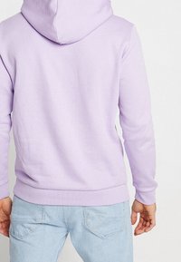 Levandulová mikina s kapucí vyrobená z měkké tkaniny, s nastavitelnou šňůrkou na kapuci, žebrovanými manžetami a lemem, s hladkou texturou a minimalistickým designem.