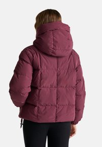 Czerwona kurtka puchowa z kapturem, z pikowanym wzorem, elastycznymi mankietami i ściągaczem u dołu. Materiał wydaje się gładki i termoizolacyjny.