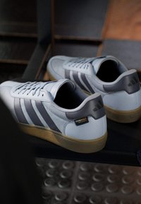 Witte en grijze sport sneakers met gestructureerde oppervlakken, voorzien van suede en leren accenten, kenmerkende drie strepen en gumrubberen zolen.